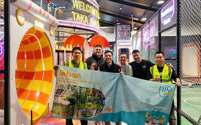 Lebanplay installation team and client representatives after completing the indoor playground project in Alicante, Spain, with interactive slides, lighting effects, and play equipment in the background.