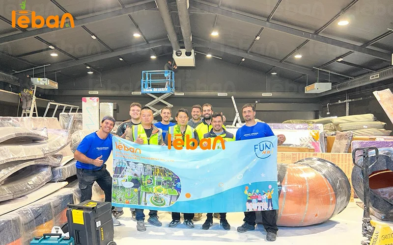 Lebanplay on-site installation team and client representatives at the Alicante indoor playground project site, surrounded by packed play equipment and installation tools.