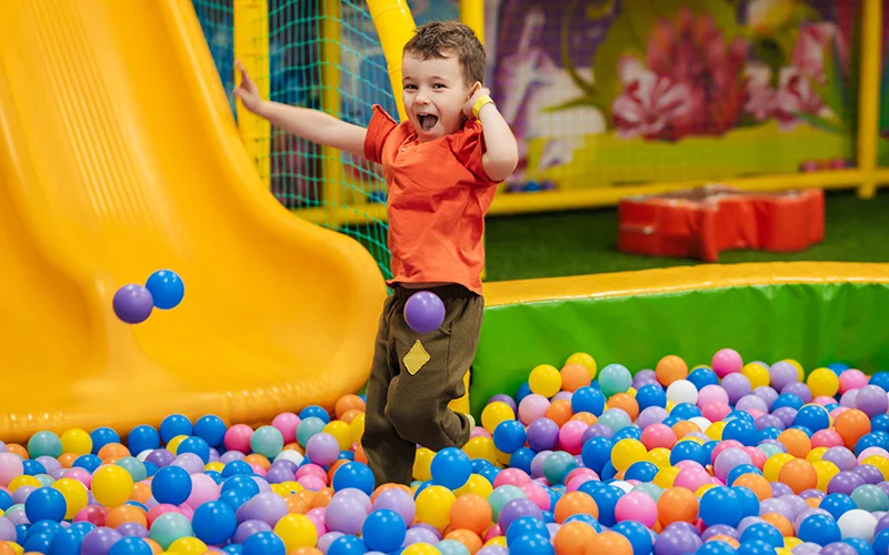 Child playing in a colorful ball pit with a slide in an indoor playground.