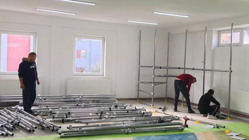 Workers assembling modular steel frames for an indoor jungle-themed playground, showing the early stage of playground installation with scaffolding and metal pipes.