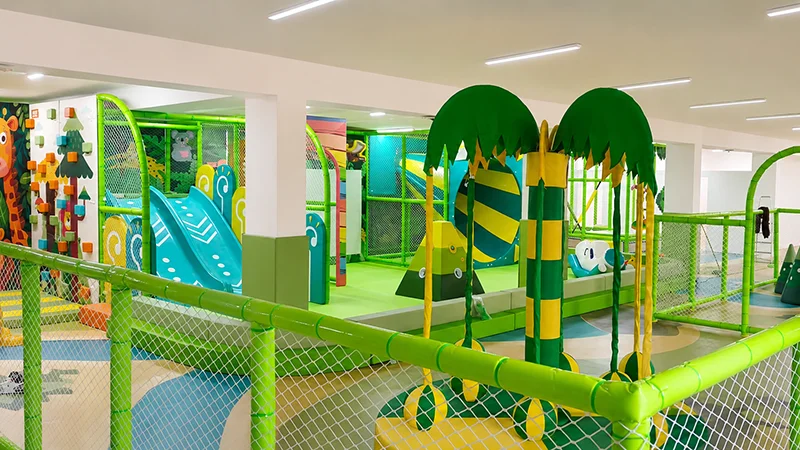 Bright jungle-themed indoor playground for children with slides, ball pit, climbing wall, and interactive play structures