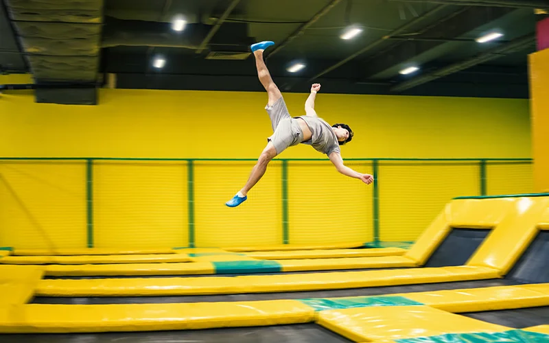 Teen boy performing acrobatic jump on indoor trampoline park yellow mats with safety nets
